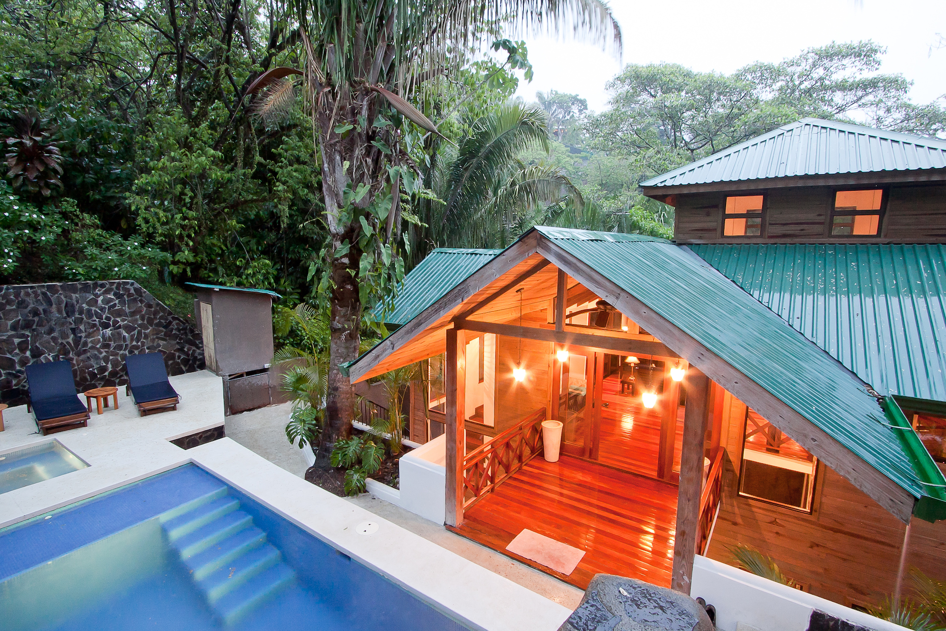 La villa de madera multinivel, con techo verde y espacios interiores cálidos, se conecta a una piscina privada y zona de jacuzzi, todo inmerso en un ambiente de selva vibrante.