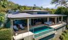 La villa contemporánea cuenta con una piscina de borde infinito que se extiende desde una amplia terraza cubierta al aire libre, situada en una ladera con vistas al paisaje circundante.